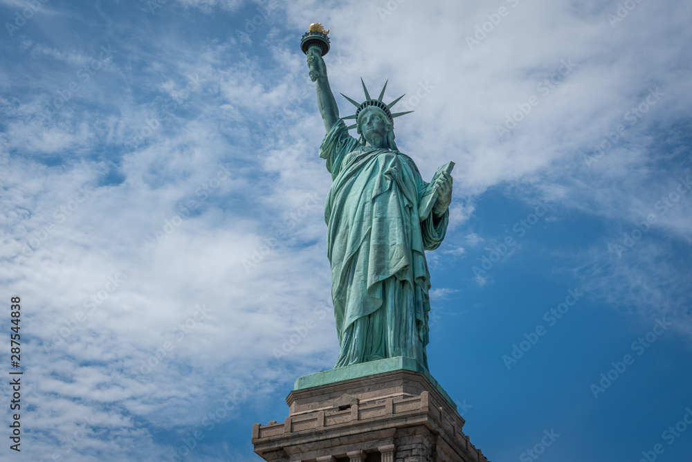 Fototapeta premium Shot of the Statue of Liberty in New York City, Usa. The shot is taken during a beautiful sunny day with a blue sky and white clouds in the background 