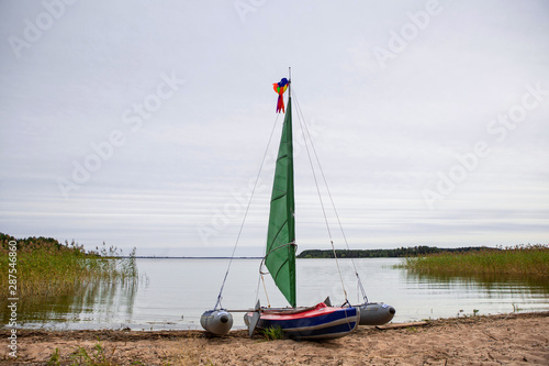 Kayak with a sail on the sandy shore. Water travel. Skyline. The banks are overgrown with reeds.