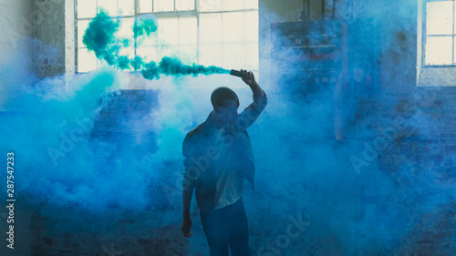 Young man holding smoke bomb in empty warehouse photo