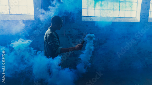 Man holding blue distress flare inside empty warehouse