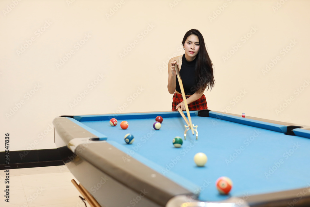 Fototapeta premium beautiful and sexy asian woman in black dress playing billiard or snooker on blue pool table with happy smiling face during holiday vacation