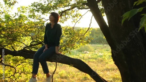 Girl sitting and swinging on a branch of a tree. Young woman in a forest having fun. 