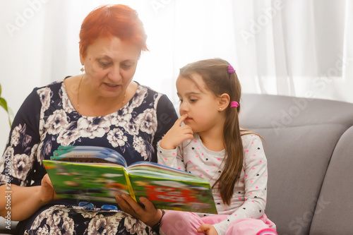 Portrait of a senior woman and a little girl stretched out on a bed reading a book photo