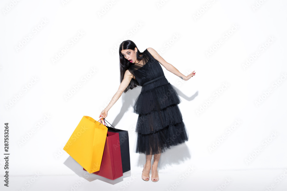 Young brunette woman in black dress shopping on white background. Attractive caucasian female model. Finance, black friday, cyber monday, sales, autumn concept. Copyspace. Shocked, astonished. Young brunette woman in black dress shopping on white background. Attractive caucasian female model. Finance, black friday, cyber monday, sales, autumn concept. Copyspace. Shocked, astonished.