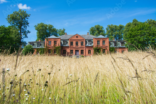 Old and abandoned mansion in Latvia, sunny day time, meadow in front photo