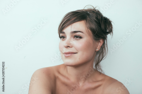 Close up of young attractive confident white woman with beautiful skin and gentle smile.  Brunette  hair up. White background.