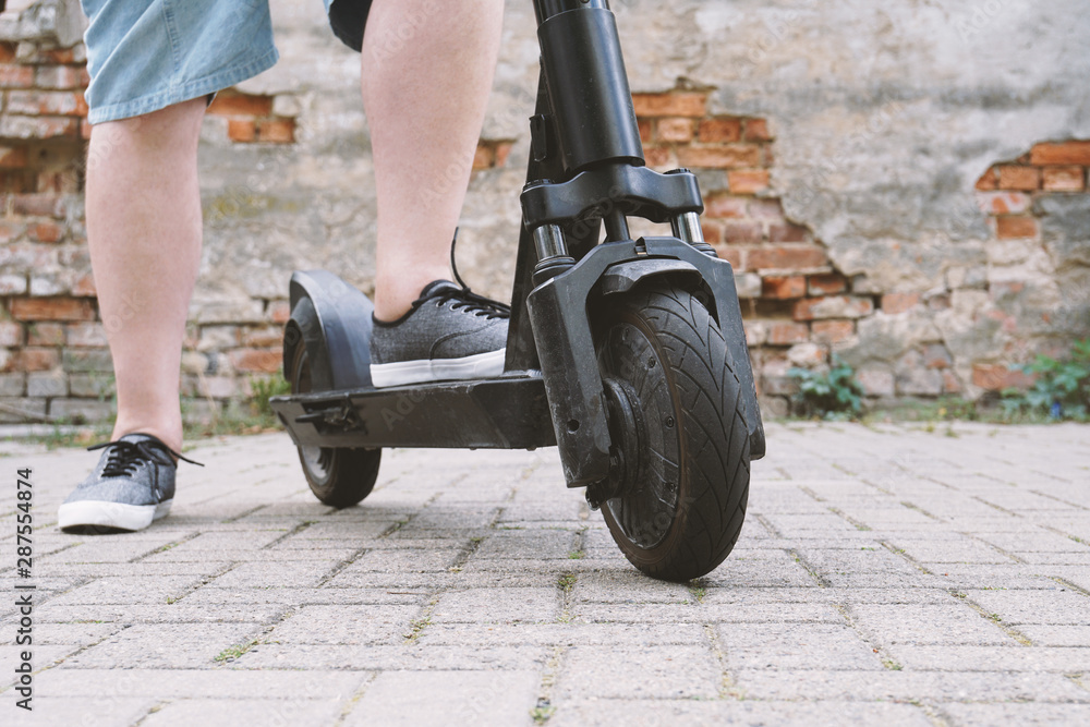 legs of unrecognizable man wearing shorts with electric kick scooter or e-scooter - e-mobility or micro-mobility hipster lifestyle trend legs of unrecognizable man wearing shorts with electric kick scooter or e-scooter - e-mobility or micro-mobility hipster lifestyle trend
