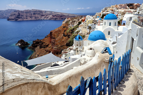 Blue fence leading to the blue domes and white buildings of Santorini looking over the blue Aegean Sea, Greek Islands