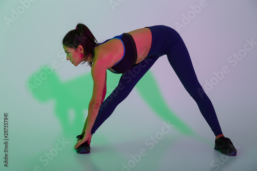 Beautiful young sports woman posing isolated with led flash lights make stretching exercises.