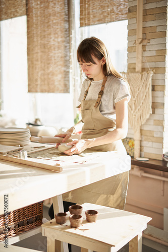 Beautiful young woman making ceramic ware, roll out with a rolling pin in sun light. Concept for woman in freelance, business, hobby