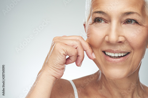 Gorgeous smiling Caucasian senior woman with short gray hair pinching her cheek. Beauty photography. photo