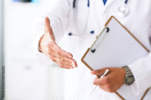 Male medicine doctor hold pad and give arm to shake in office closeup. Friend welcome introduction or thanks gesture. Work examine patient congratulation help exam teamwork deal concept.