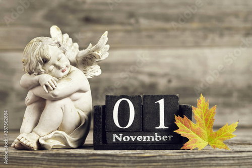All Saints Day. Angel, wooden calendar and yellow autumn leaf photo