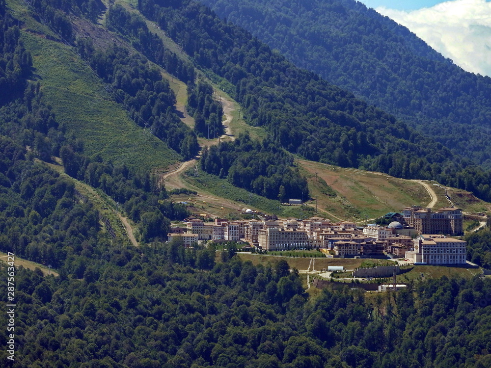 ski resort hotels surrounded by green forest in a mountain valley at the foot of the high Caucasus mountains on a summer sunny day