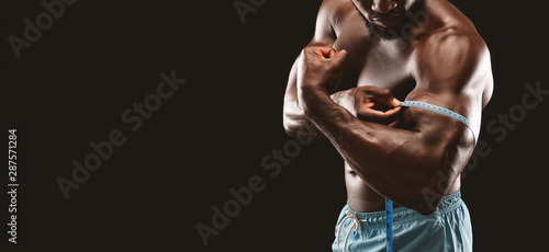 Cropped image of athletic african guy measuring his biceps
