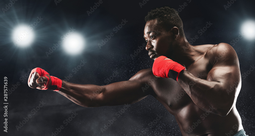 Side view of professional black man fighting on boxing arena