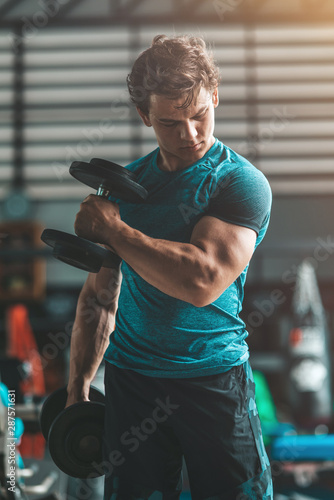 Obraz na płótnie Portrait of caucasian athletic man holding two dumbells at once and showing his muscular arm