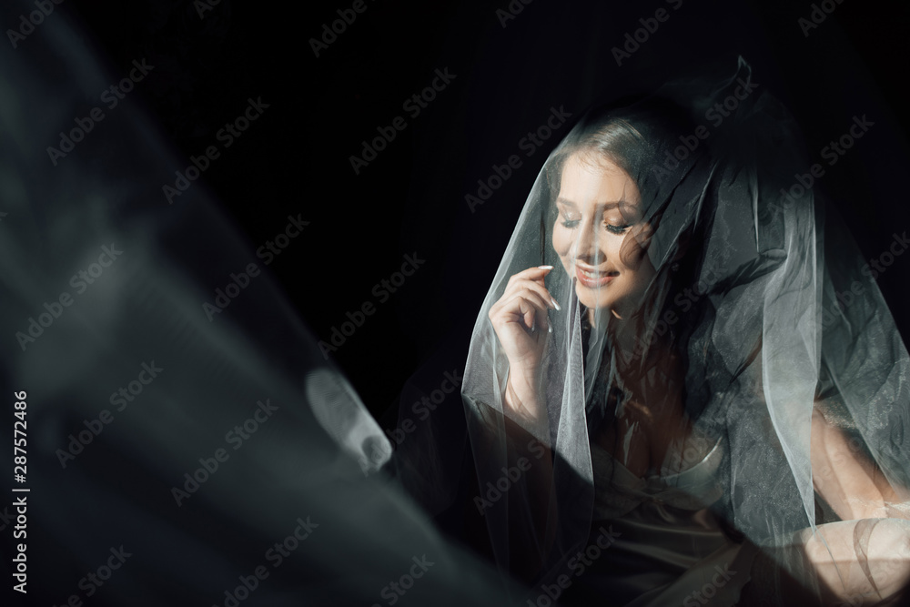 Portrait of charming bride enveloped in a veil. Beuatiful bride hidden under the veil. Beautiful bride in veil. Close up. Beauty woman. Wedding morning closeup on black background. Portrait of charming bride enveloped in a veil. Beuatiful bride hidden under the veil. Beautiful bride in veil. Close up. Beauty woman. Wedding morning closeup on black background.
