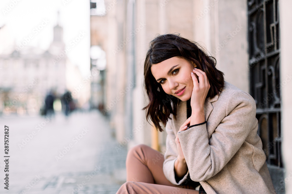 Street portrait of young beautiful happy smiling woman wearing stylish coat and pants. Model looking at camera. Female fashion concept. Copy space, free text