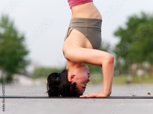 Quadro em tela Side view of healthy women in sportswear, red pants and top practicing yoga outdoor, doing headstand exercise on yoga mat salamba sirsasana pose, close up portrait