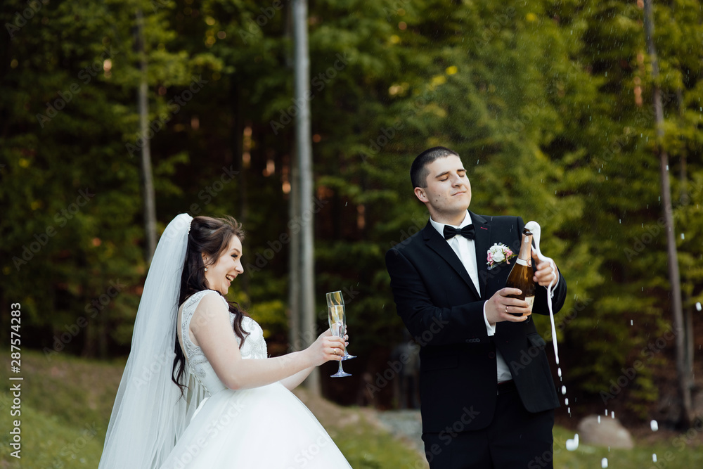 Newlyweds clinking glasses and enjoying romantic moment together. The groom uncovers champagne. Wedding. The champagne glasses.  Happy bride and groom on their wedding day.