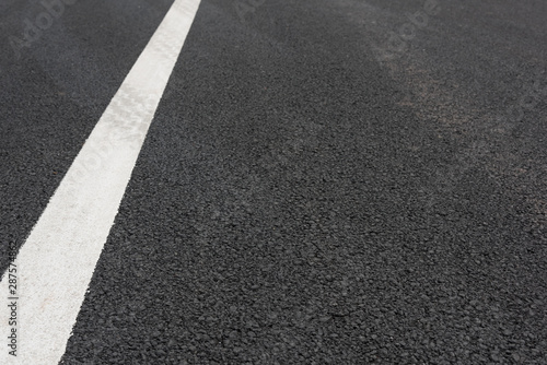 Low angle view of a white paint slash on black asphalt road © bqmeng