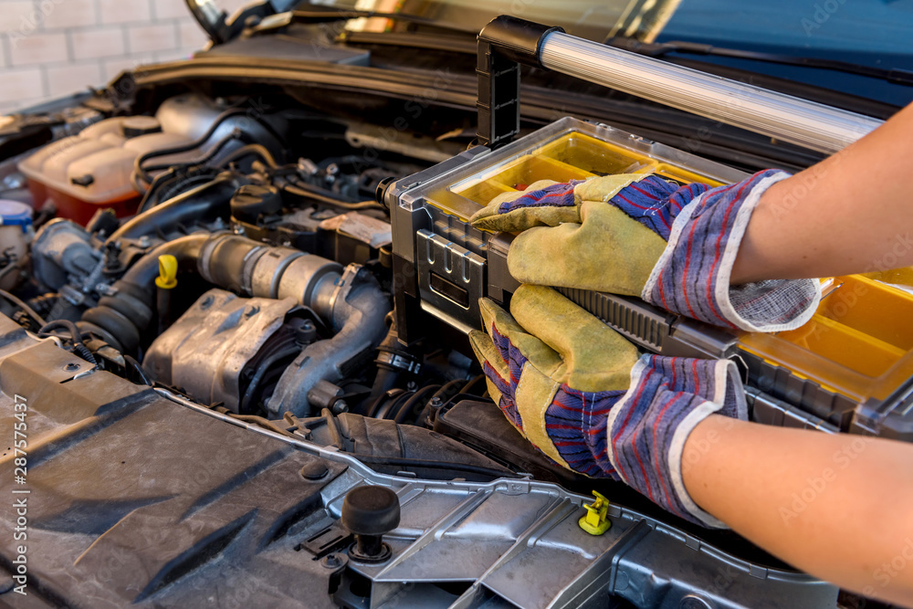 Mechanic holding tool box near broken car