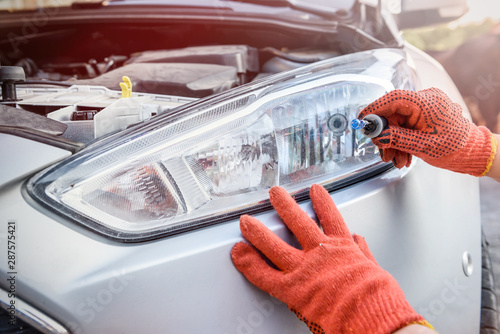 Mechanic holding lamp and cables from headlamp of car photo