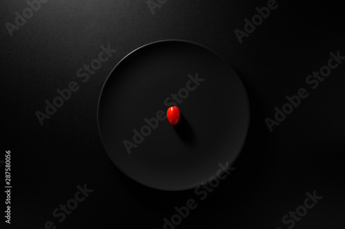 One cherry tomato served in black plate on moody black background. Top view. Healthy diet concept.