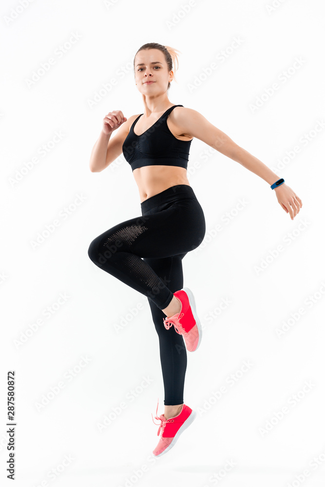 Young sporty blond woman in a black sportswear jumping isolated over white background. Sport activity