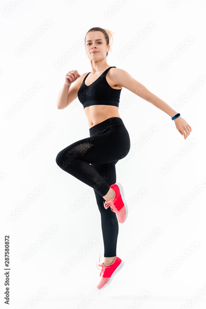 Young sporty blond woman in a black sportswear jumping isolated over white background. Sport activity Young sporty blond woman in a black sportswear jumping isolated over white background. Sport activity