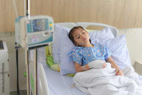 Patient child laying on hospital bed with blurred saline solution drip and infusion pump equipment