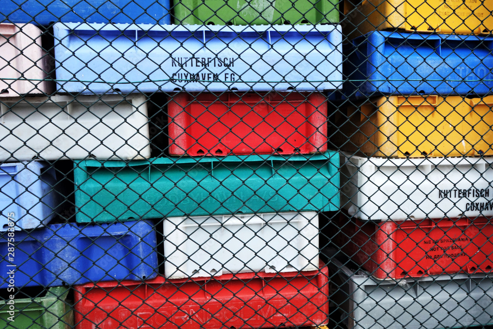 stacks of multicolored plastic boxes used by fishermen at the Baltic Sea stacked behined wire mesh fence at fish factory