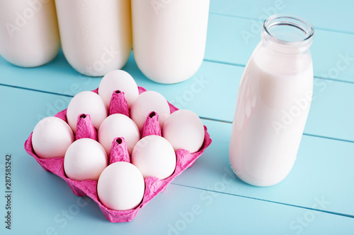 Bottle of milk and white eggs in a pink filler tray on turquoise wooden country kitchen table. Close up ciew from above photo