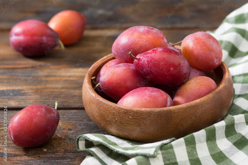 Red plums in a wooden bowl on a wooden table. Rustic style Red plums in a wooden bowl on a wooden table. Rustic style