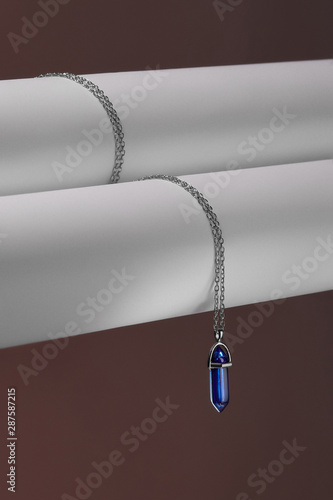 Close-up shot of a steely chainlet with a pendant in the form of screw with a fitted-in indigo-blue gemstone similar to a lazulite. The gemstone is elongated and conical.  photo