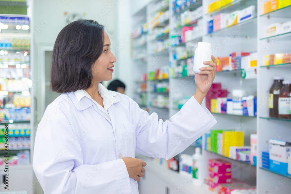Asian pharmacist is checking the medicine on shelves in pharmacy. Health care and medical concept.