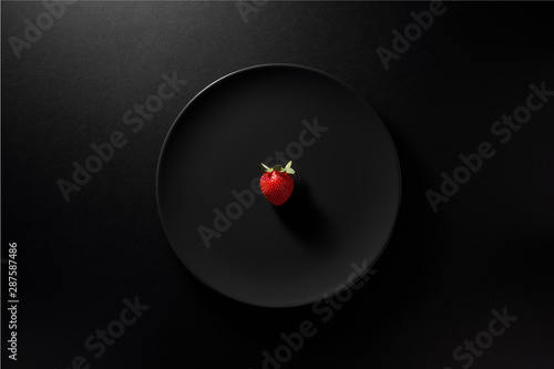 One fresh strawberry served in black plate on moody black background. Top view. Healthy diet concept.