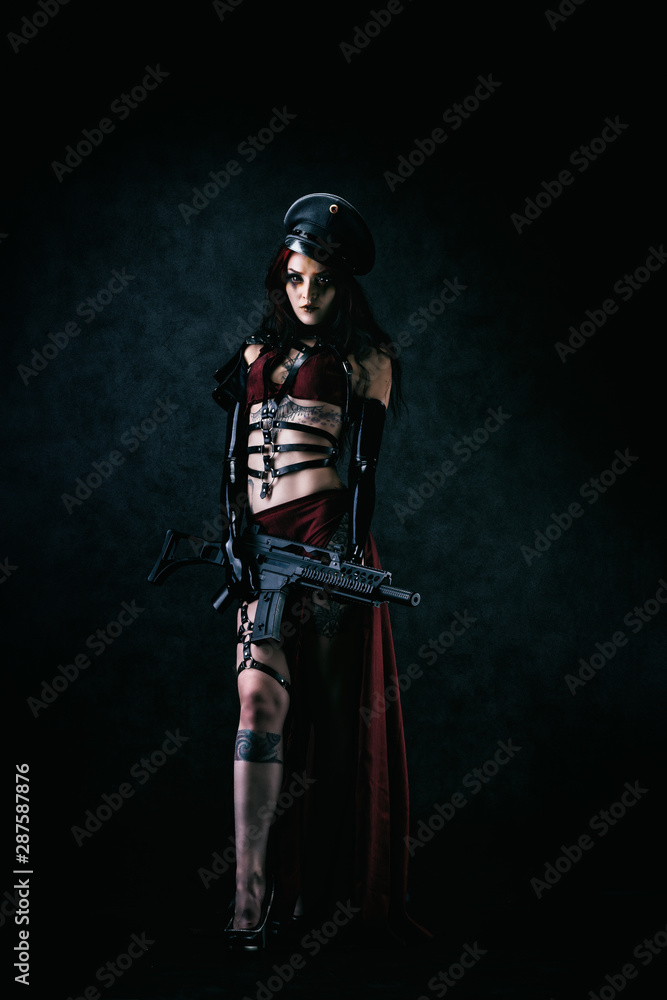 Young black-eyed Cyborg in leather armor and a cap holding a machine gun in his hands Young black-eyed Cyborg in leather armor and a cap holding a machine gun in his hands