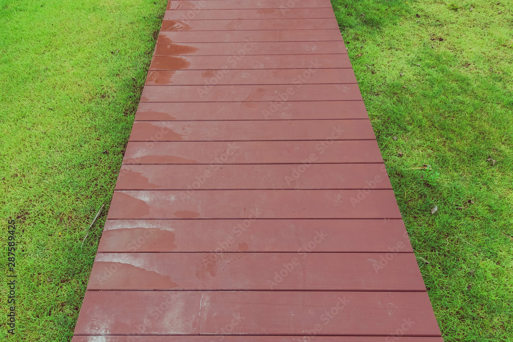The reddish brown wooden walkway after rain in the garden.