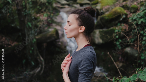 Young woman practicing breathing yoga pranayama outdoors in moss forest on background of waterfall. Unity with nature concept. photo