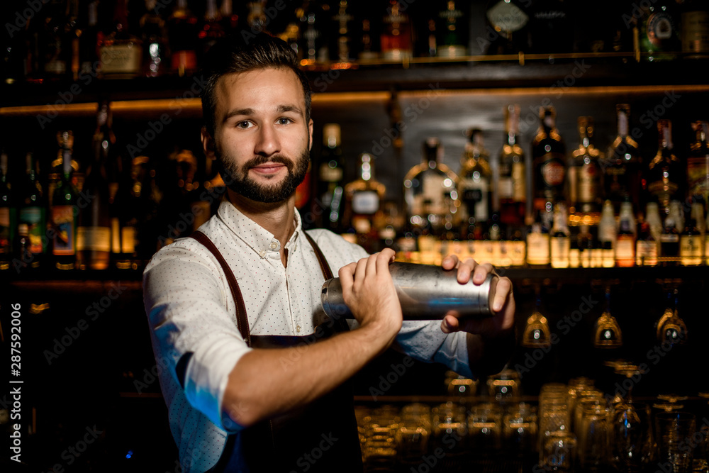 Smiling bartender standing with a professional steel shaker making a cocktail