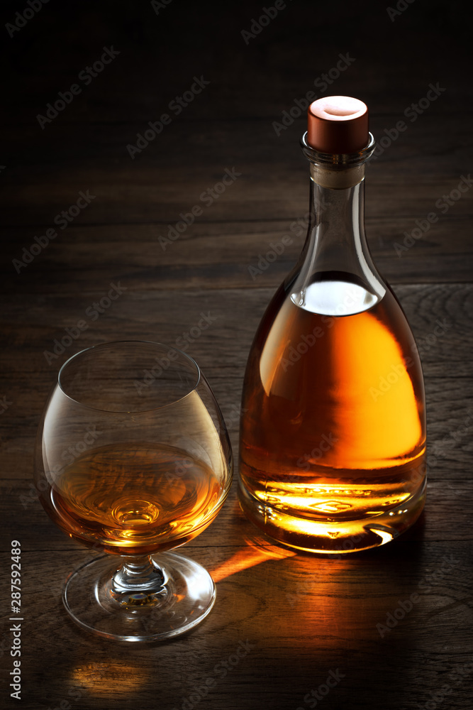 view of glass of cognac and a bottle aside on color wooden background. view of glass of cognac and a bottle aside on color wooden background.