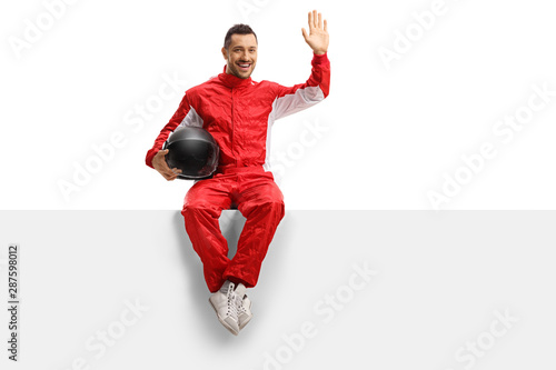 Young man racer in a red uniform sitting on a panel and waving