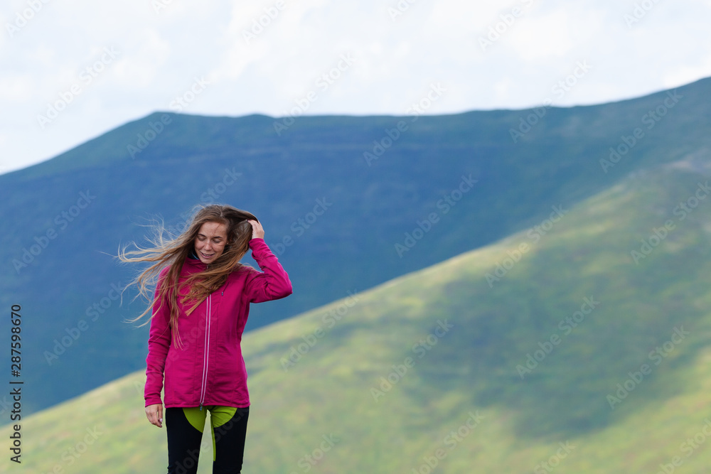 Portrait of smiling girl while straightening hair in wind in the mountains.