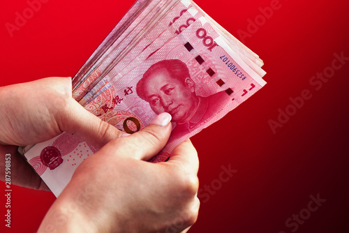 A pile of RMB banknotes of Chinese yuan money in a female hand on a red background photo
