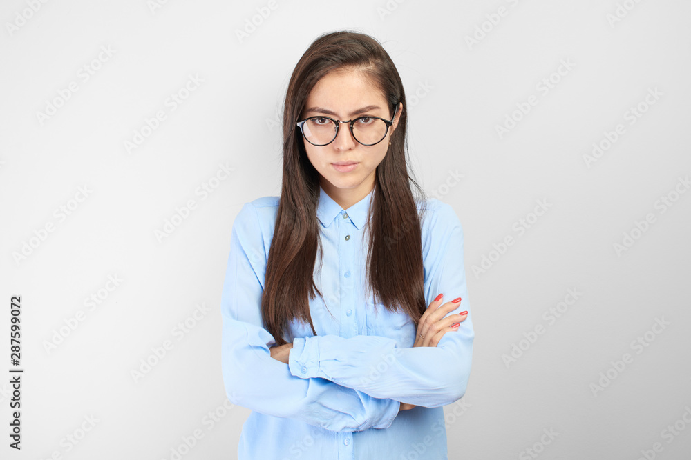 Offended Asian Kazakh nerd student girl with displeased face and arms folded in glasses looks upset at the camera in white studio isolated Offended Asian Kazakh nerd student girl with displeased face and arms folded in glasses looks upset at the camera in white studio isolated