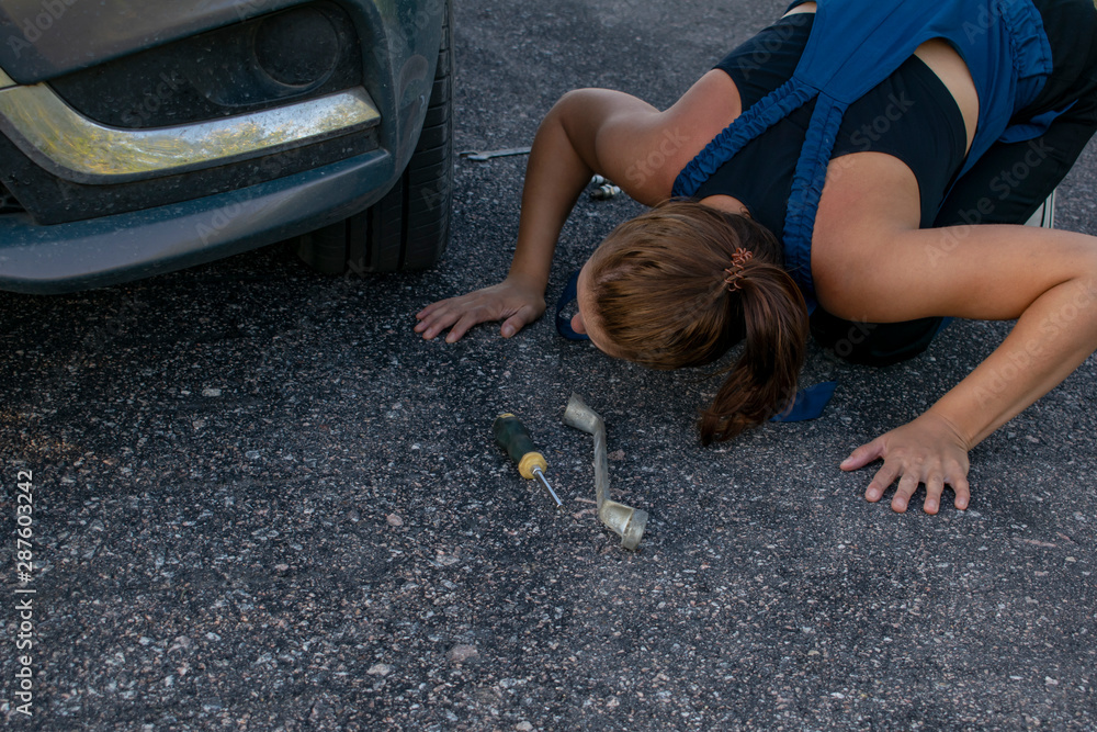 Naklejka premium Young beautiful lady mechanic with wrenches trying to fix the car on the road.