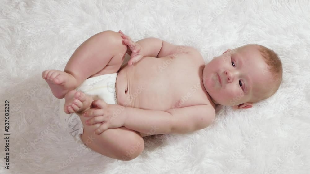 Beautiful baby is smiling. Very attractive baby lies on a white bedspread and laughs, diaper pants. Close-up Beautiful baby is smiling. Very attractive baby lies on a white bedspread and laughs, diaper pants. Close-up