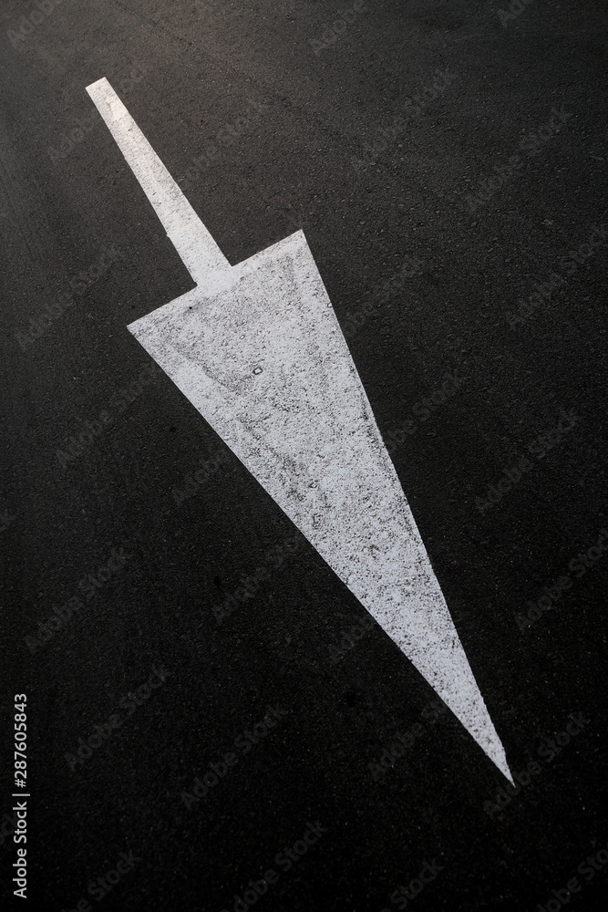 Fototapeta premium Long white arrow on black background, diagonal composition, angled perspective, vertical frame.